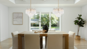 Two elegant glass pendant chandeliers with gold accents, available at Franklin Lighting, hang over a modern dining room table, casting a warm and inviting light