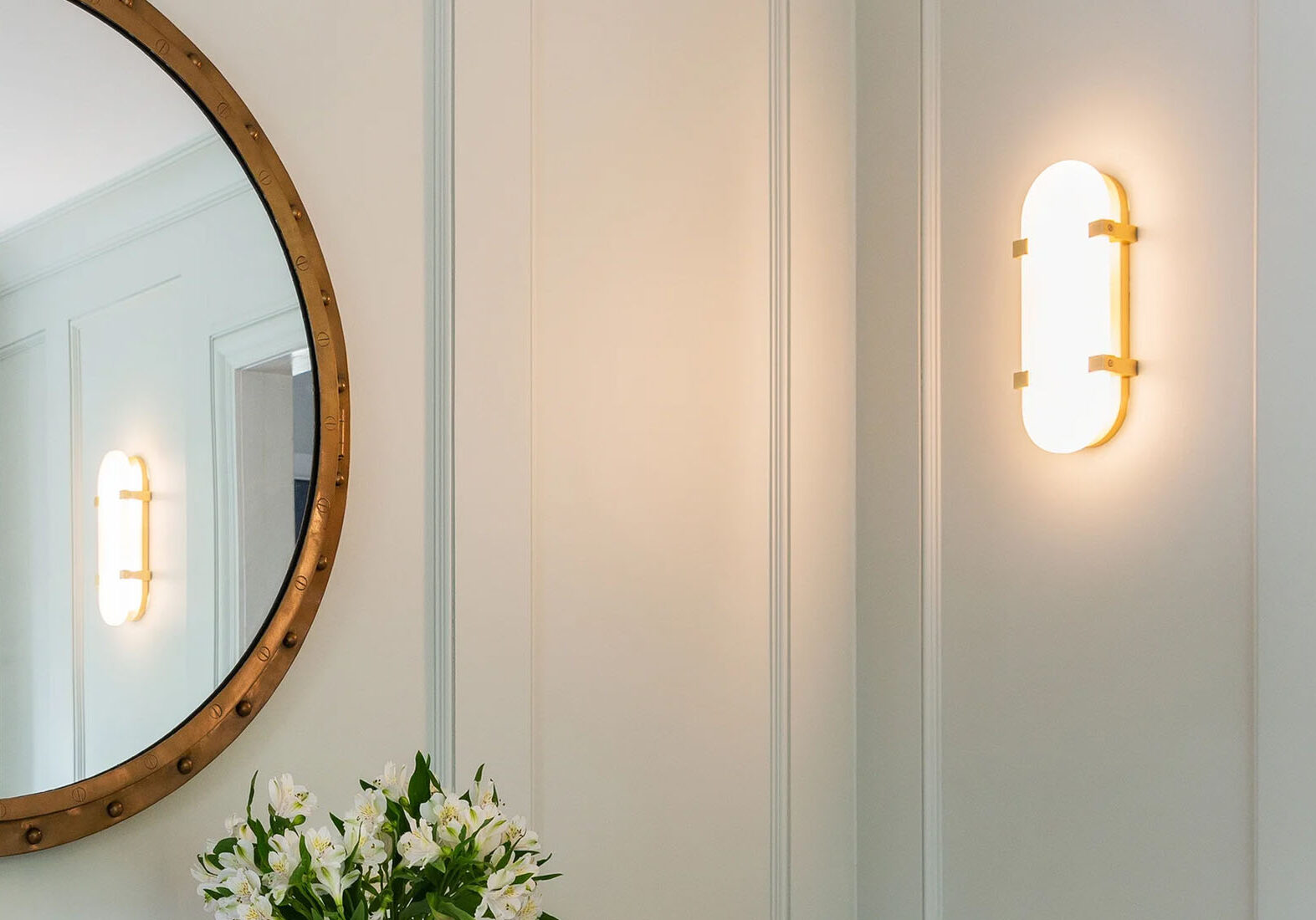 Elegant glass wall sconce mounted on a light blue paneled wall with a gold mirror.