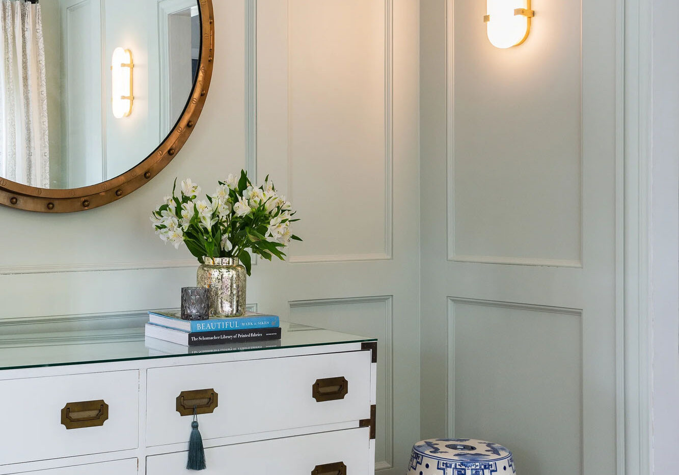 Elegant vanity lighting featuring a handcrafted vertical gold wall sconce and round mirror.